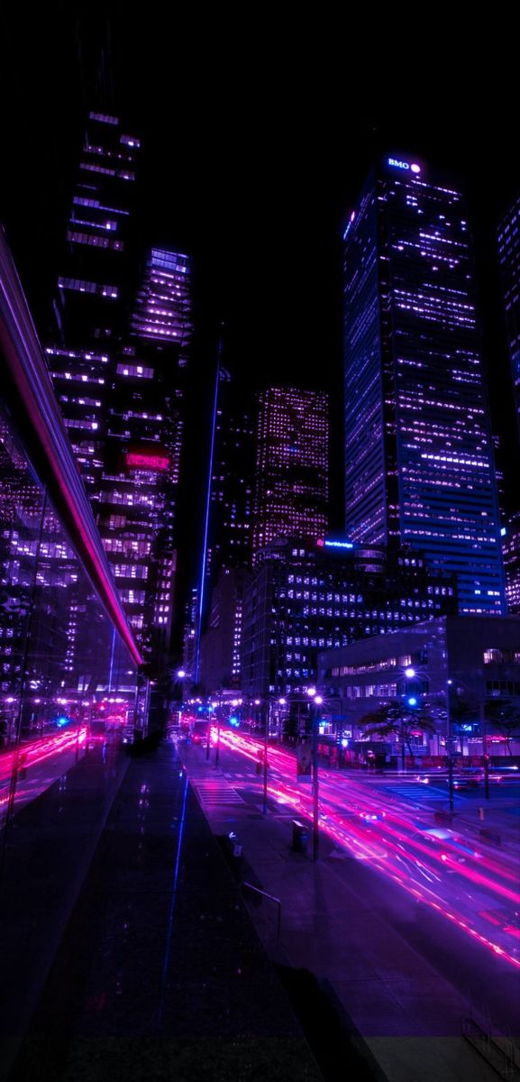 the city skyline is lit up at night with bright lights in the foreground and blurry traffic on the street