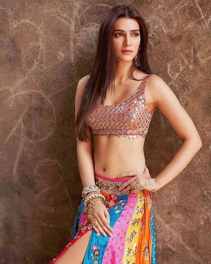 a beautiful young woman in a colorful skirt and top posing for the camera with her hands on her hips