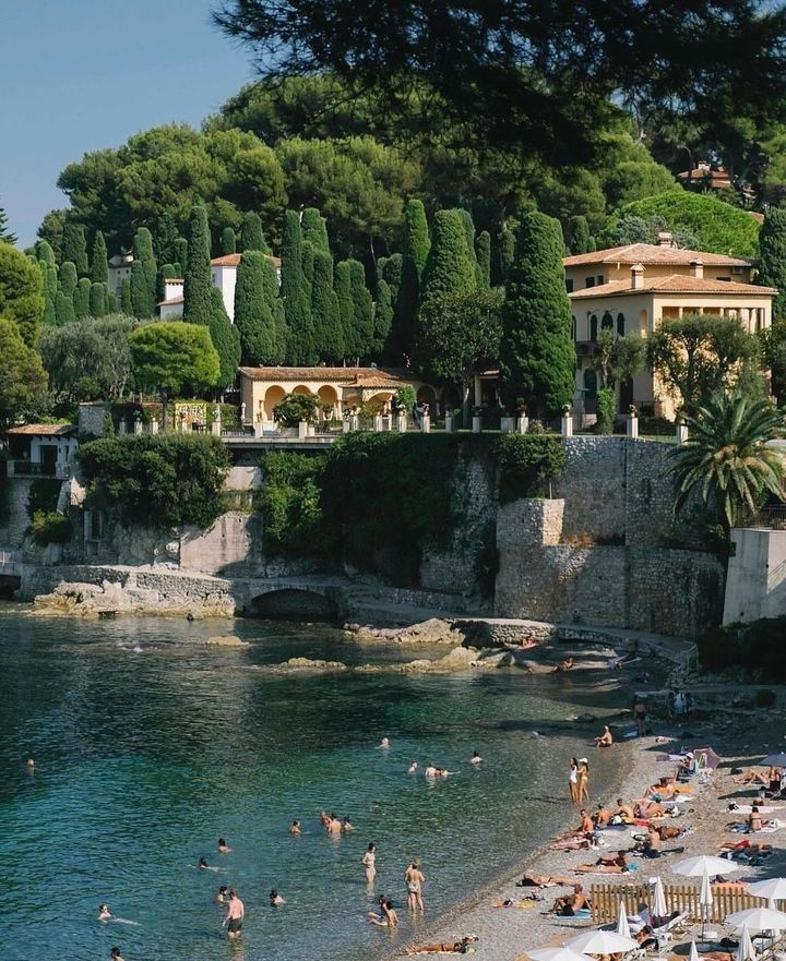 many people are on the beach in front of some houses and trees, while others swim