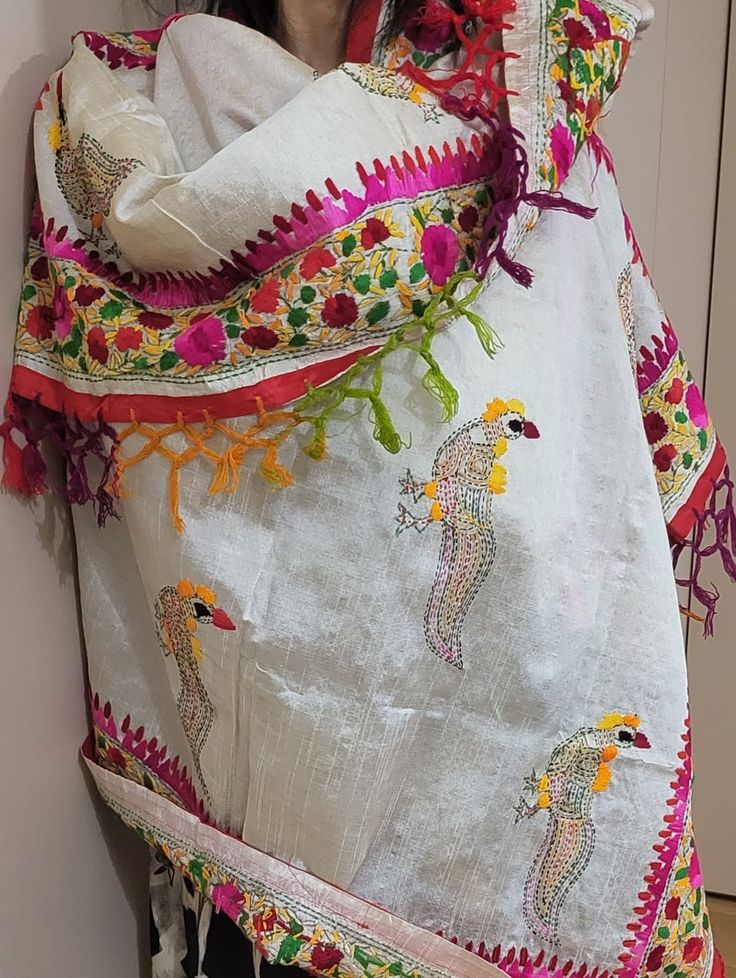 the woman is wearing a white shawl with colorful embroidered designs on it and holding her hands behind her back