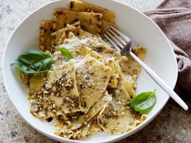 a white bowl filled with pasta covered in pesto and parmesan cheese next to a fork