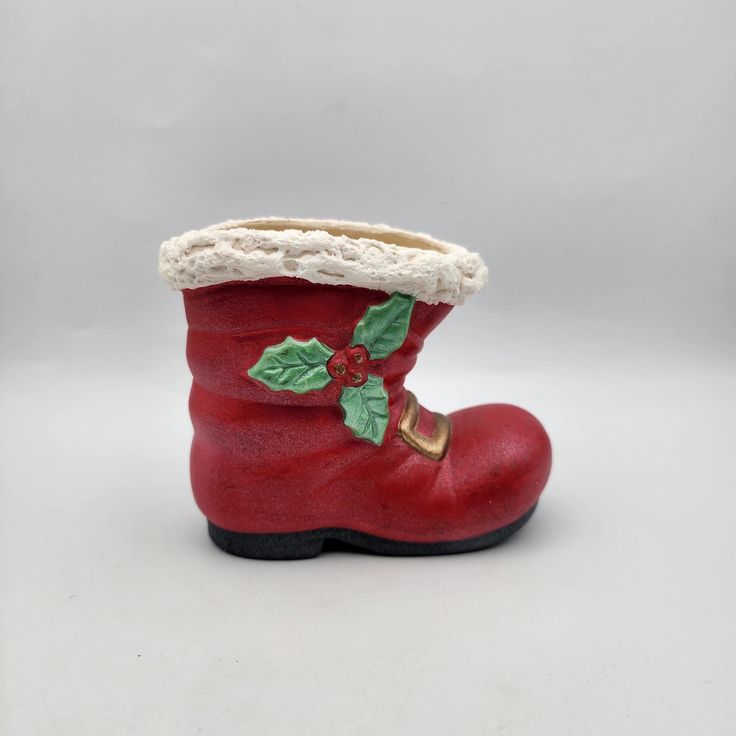 a red boot with holly leaves and a white lace on the top is sitting in front of a gray background