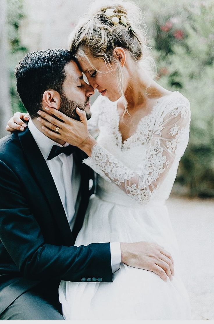 a bride and groom are sitting on the ground together, embracing each other with their arms around one another