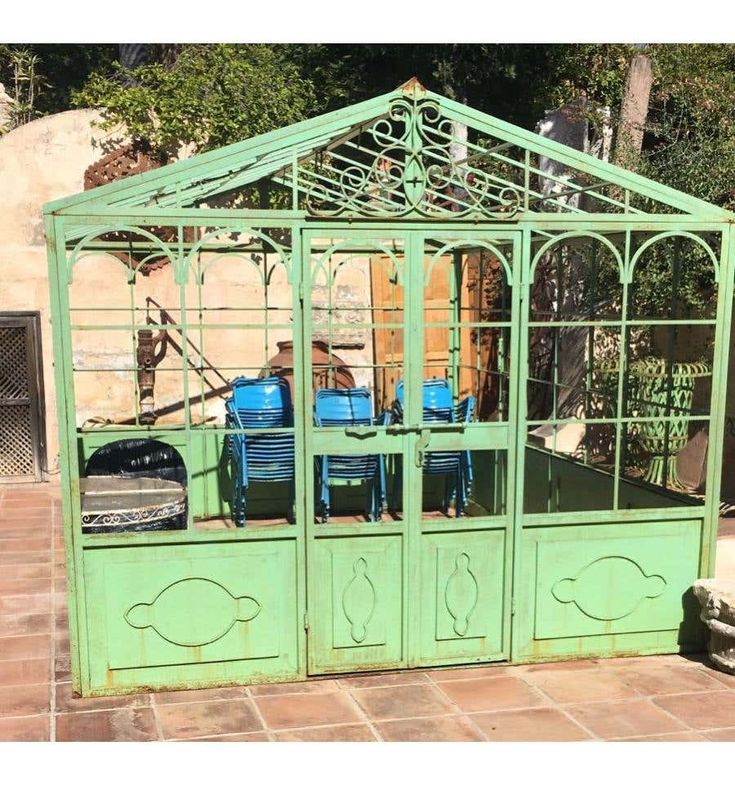 a green metal gazebo sitting on top of a brick floor next to a building