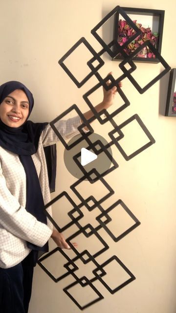 a woman standing in front of a wall with an art piece hanging on it's side