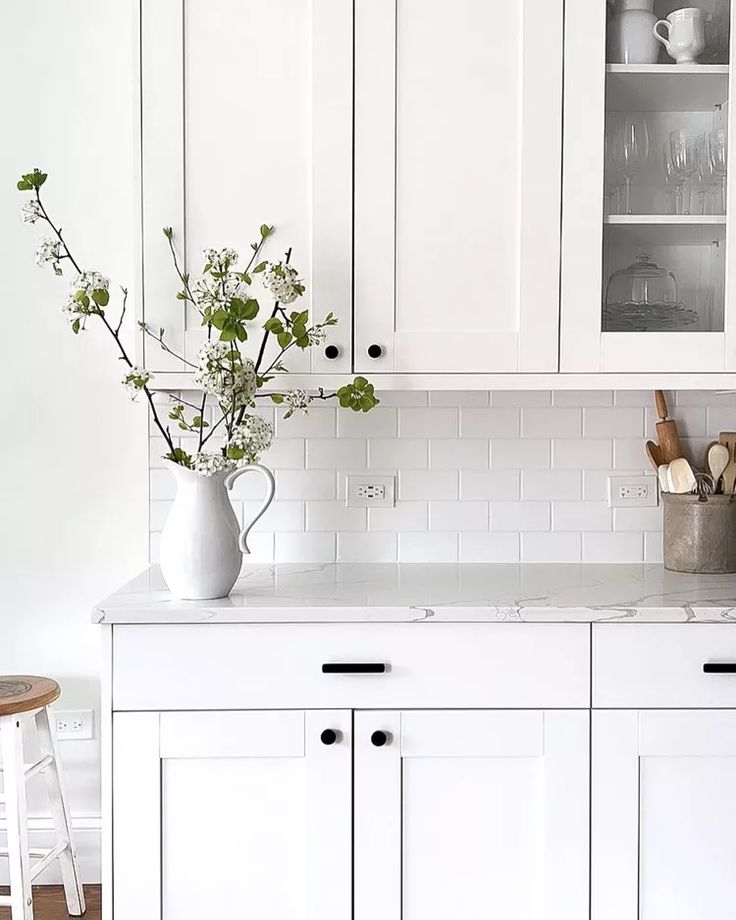 a kitchen with white cabinets and wooden stools next to a vase filled with flowers