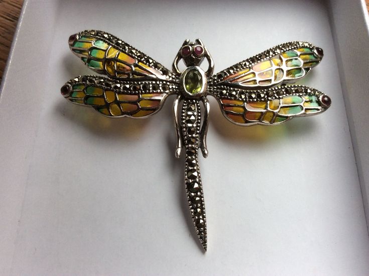 A very pretty vintage Art Nouveau style sterling silver dragonfly brooch or pendant. The amber and green coloured plique-a-jour wings are decorated with sparkling marcasites and tiny cabochon rubies at their tips. The eyes are tiny cut rubies and the thorax is a bezel set cut peridot stone measuring 5 mm x 3 mm. The tail is also decorated with marcasites. The brooch has a roll over safety catch and it has a pendant loop. The back is marked 925 for sterling silver. This item is in very good used Handmade Silver Costume Jewelry Brooches, Sterling Silver Green Brooch, Green Sterling Silver Brooch Jewelry, Green Sterling Silver Brooch, Green Sterling Silver Brooch For Gift, Green Sterling Silver Brooches As Gifts, Green Sterling Silver Brooches For Gifts, Art Nouveau Silver Brooch, Elegant Green Dragonfly Shaped Jewelry