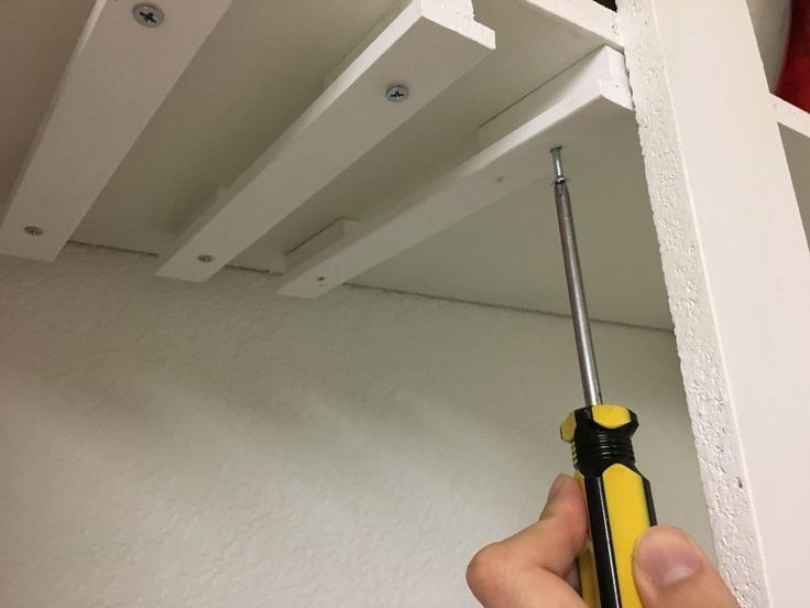 a hand holding a screwdriver in front of a shelf with shelves on it