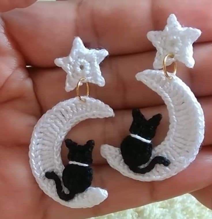 small black cat sitting on the moon shaped crochet earrings in white and gold