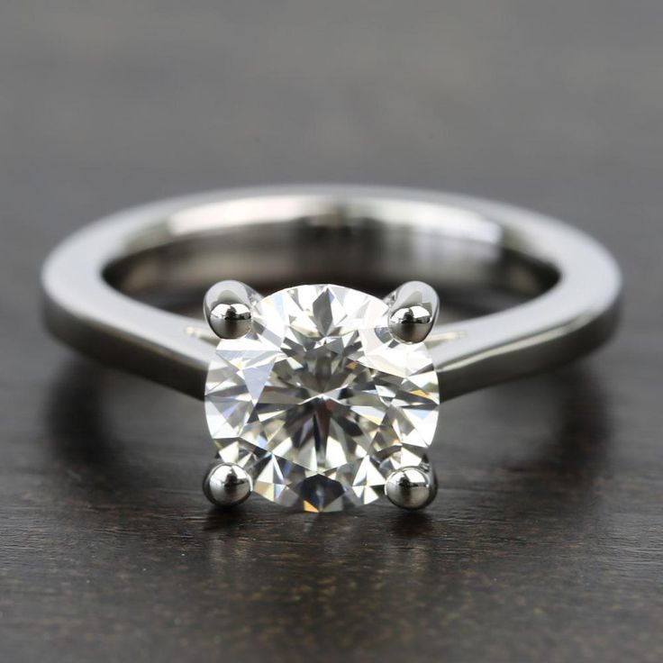 an engagement ring with a round brilliant cut diamond set in the shans, on a wooden surface