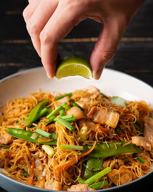 a person is tossing a lime into a bowl of noodles with chicken and asparagus