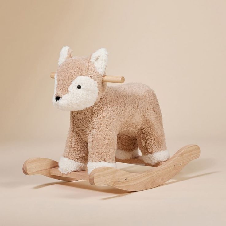 a small stuffed animal on a wooden rocking horse with white fur and black nose, sitting in front of a beige background