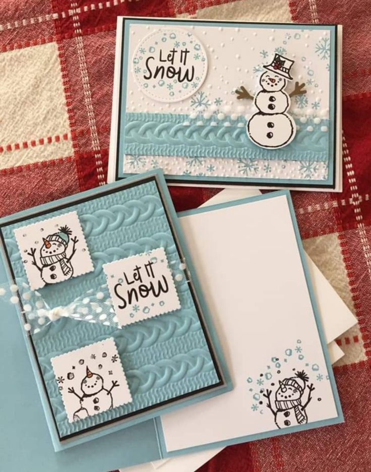 two cards with snowmen on them sitting on top of a plaid cloth covered tablecloth