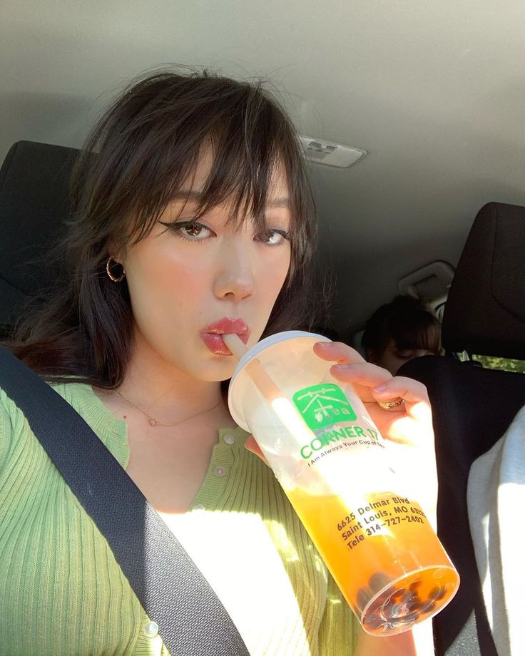 a woman drinking from a bottle in the back seat of a car