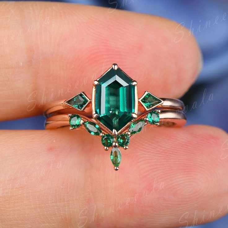 a close up of a person's hand holding an emerald ring