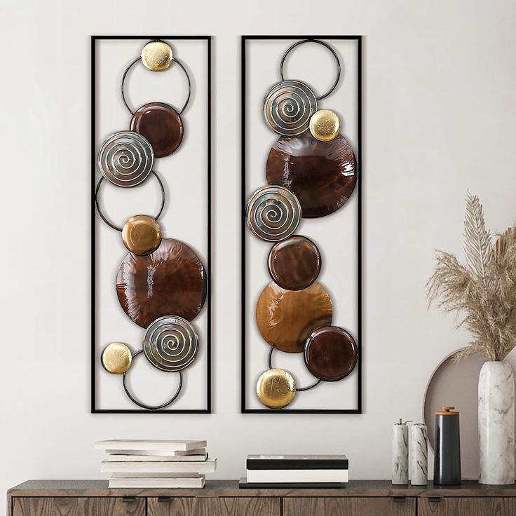 two metal wall art pieces sitting on top of a wooden dresser next to a vase