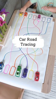 a young boy sitting in front of a table with cars on it and the words car road tracing