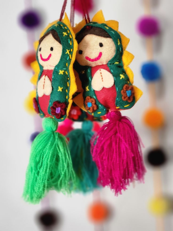 two little dolls hanging from a string with tassels on it's sides