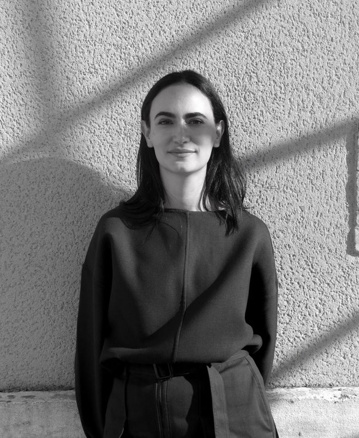 a black and white photo of a woman standing in front of a wall with her hands on her hips