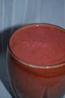 a glass filled with red liquid sitting on top of a blue table cloth next to a white wall