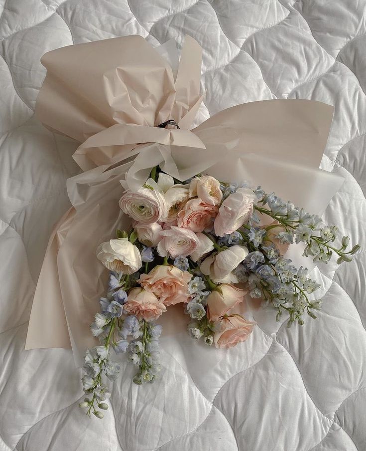 a bouquet of flowers laying on top of a white quilted bed sheet with a bow