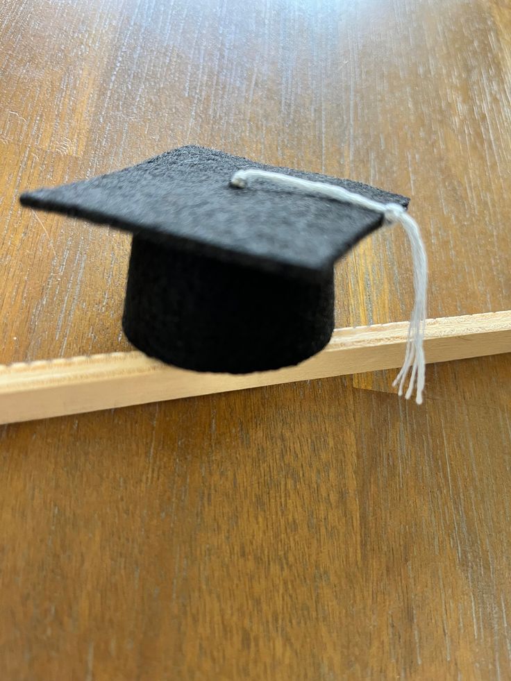 a black graduation cap sitting on top of a wooden floor next to a piece of wood