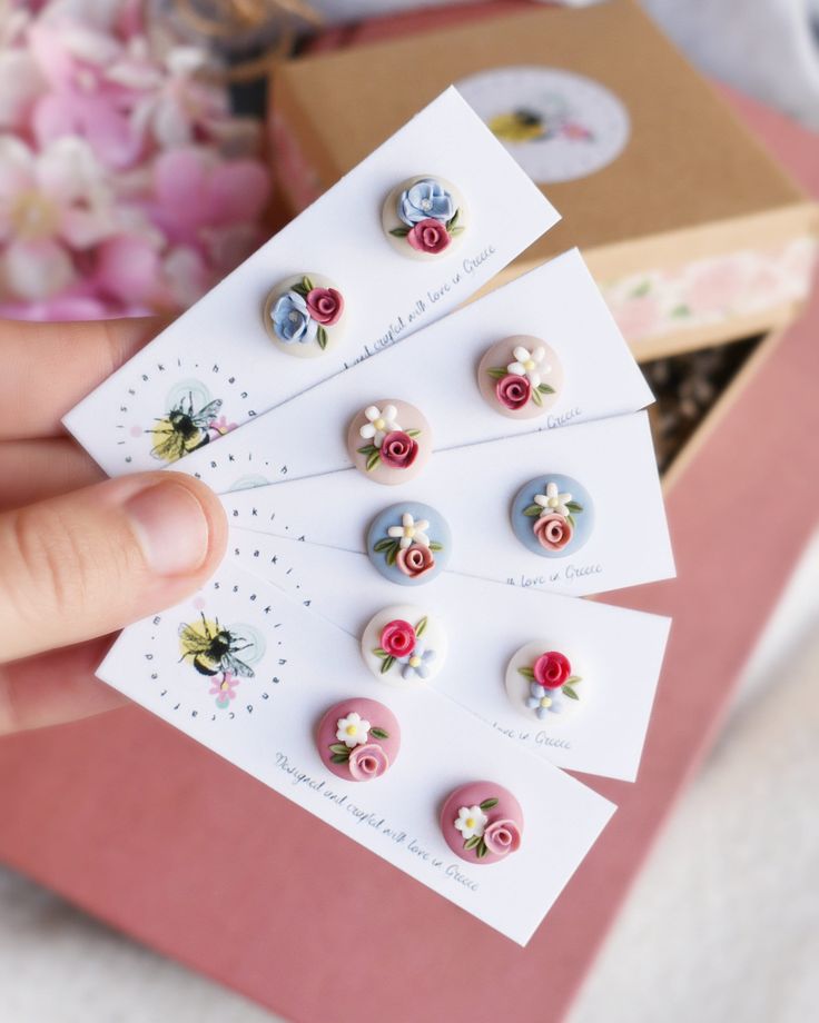 a person holding several small flowered buttons in front of a box full of flowers