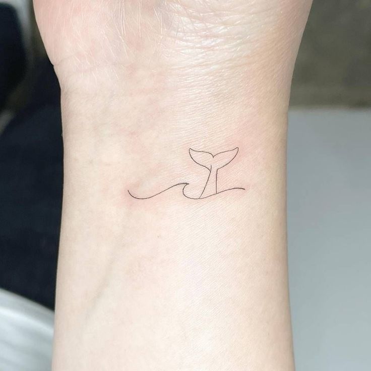 a small tattoo on the wrist of a woman's left arm with a whale tail