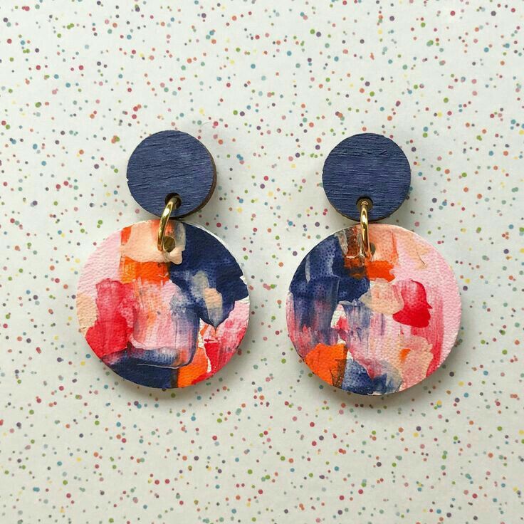 two circular wooden earrings with painted flowers on them, one is blue and the other is pink