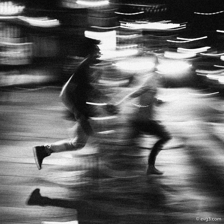 black and white photograph of people walking down the street at night with blurry lights