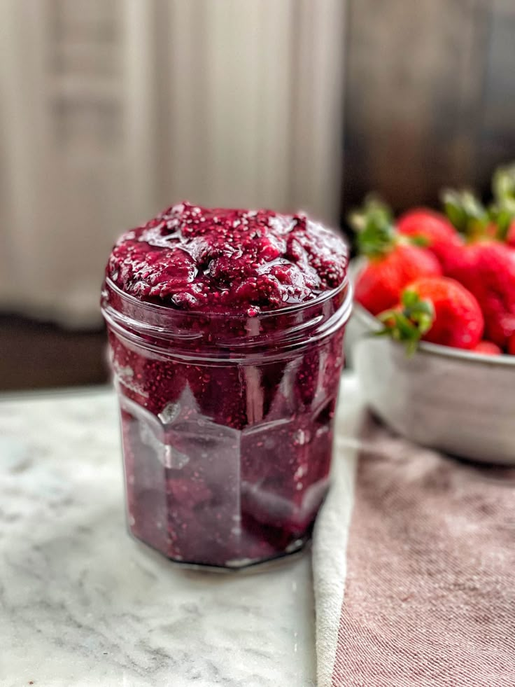 a jar filled with fruit sitting on top of a table next to bowls of strawberries