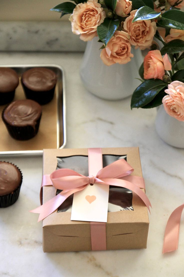 some cupcakes are sitting on a table next to flowers and a vase with roses