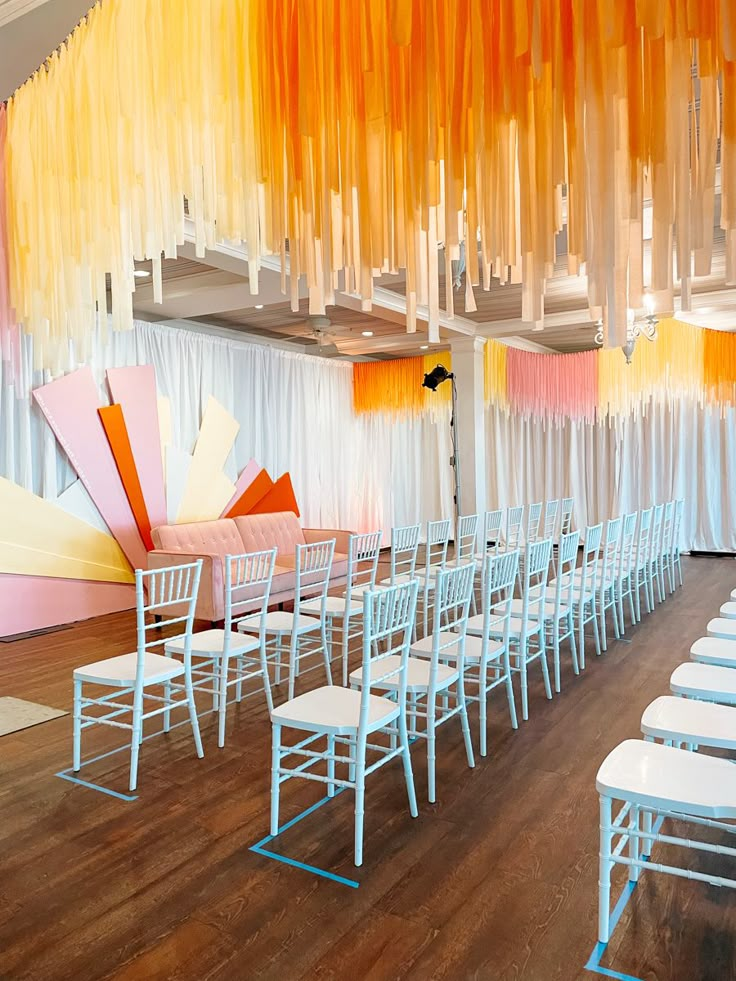 the room is set up for a wedding with white chairs and orange drapes hanging from the ceiling