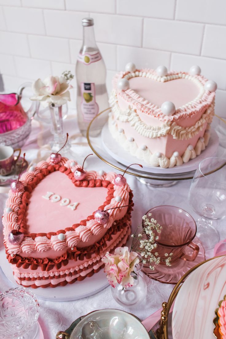 two heart shaped cakes sitting on top of a table covered in pink frosting and other desserts