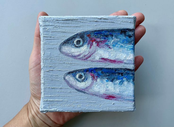 two fish painted on a piece of wood in someone's hand