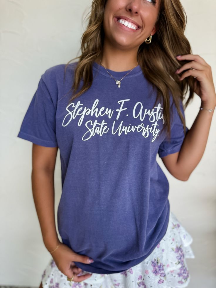 Who doesn't love representing our favorite college "Stephen F Austin" ?!?! The SFA Cursive Tee features a purple base with a front graphic. Designed with a comfort colors tee which is every college kid's favorite! Paired with our Serena Star Sneakers. Fit: Unisex, T Shirt Fabric: 100% Cotton Model is wearing a Large. She is 5’5. Bust size 32. Bra size 32A. Pants size 3. Small - fits numeric sizes 2-6 Medium - fits numeric sizes 6-8 Large - fits numeric sizes 8-12 X-Large - fits numeric sizes 12- Collegiate Screen Print Top For Campus, Collegiate Style Screen Printed Tops, Collegiate Style Screen Print Tops For Campus, Relaxed Fit Lettering Tops For Campus, Casual Tops With Lettering For Campus, Casual Campus Tops With Lettering, Casual Letter Print T-shirt For Campus, Casual Screen Print Tops For College Events, Casual Screen Print Tops For College