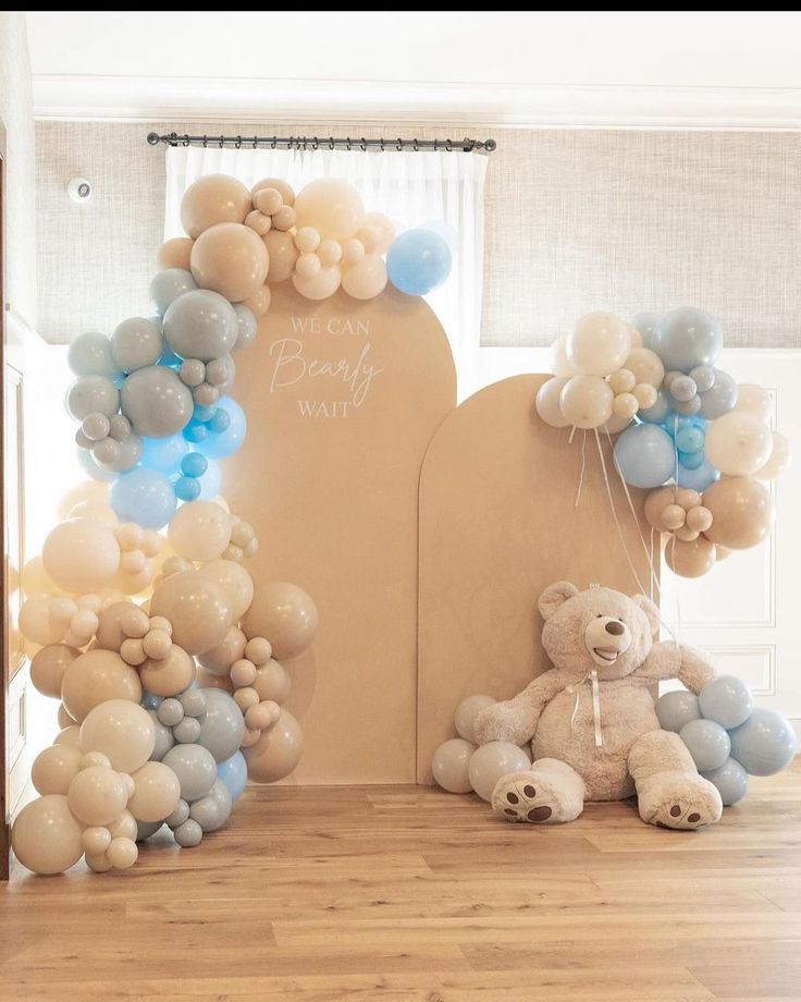 a teddy bear sitting in front of a balloon arch with blue and white balloons attached to it