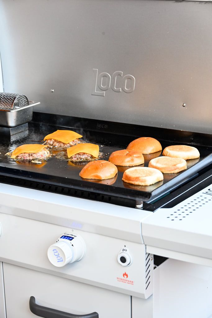 hamburgers are being cooked on an outdoor gas grill with the door open to allow more food