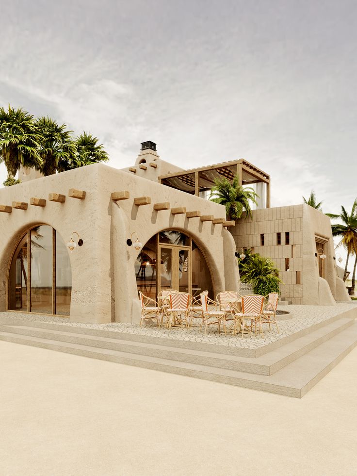 an adobe - style house with tables and chairs in front of it on the beach