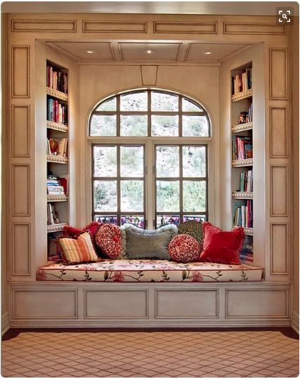 a window seat with pillows on it in front of a bookshelf