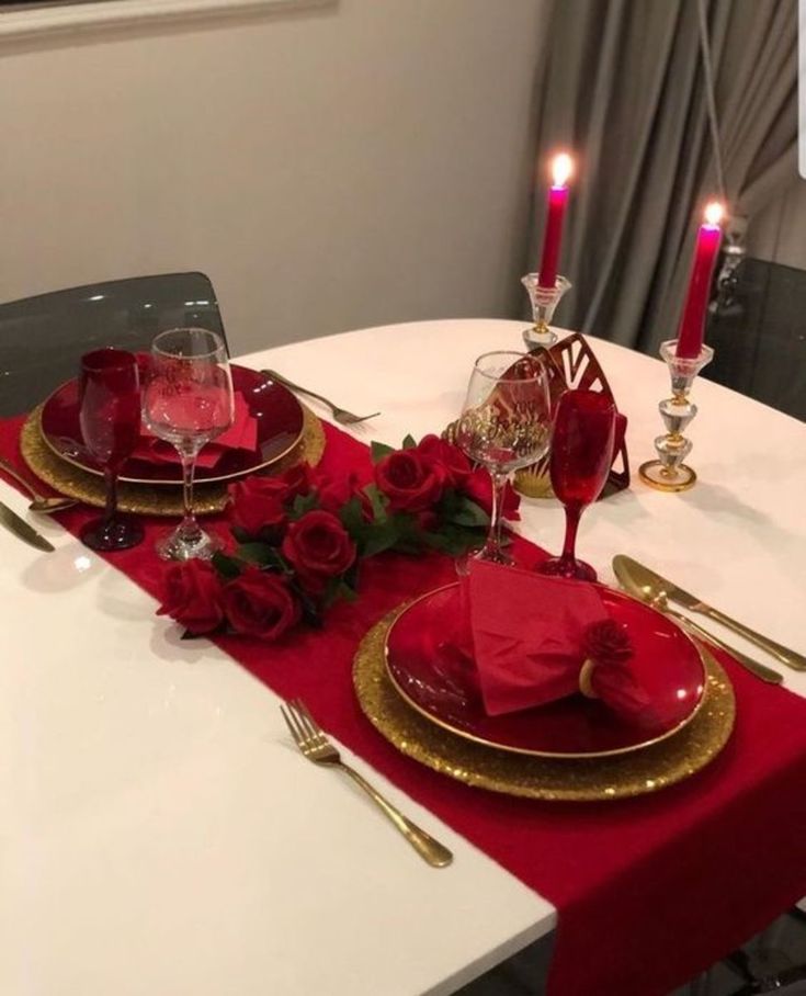 the table is set with red roses and gold place settings for two people to sit at