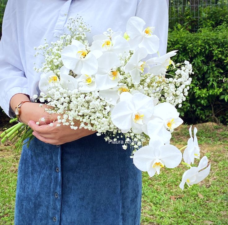 a woman holding a bouquet of white flowers in her hands and wearing a blue skirt