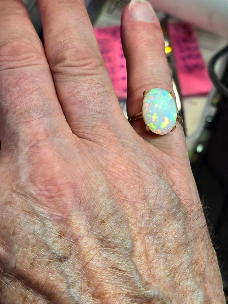 Very large  bright and  beautiful, I can't help imagining an Australian white opal of this size and color, you would need a second mortgage to own it, the only difference is you shouldn't get it wet for extended period of time. I have now sold literally thousands of opals and only a couple complaints of chafing. Large oval white  fire opal 12x18mm 8cts. Mounted on a large simple solitaire solid 14k gold ring, I like the simplicity and solidness of this ring. It's heavy for its size. Prongs will be set when the ring size is determined. Sizes available 4 thru 9. quarter and half sizes too , just leave a note and i will confirm, 20 to 40$ extra, and a little longer wait. Feel free to message me, I'm usually at my shop.. Classic Cabochon Opal Ring, Yellow Gold Ethiopian Opal Ring In Oval Shape, Classic Ethiopian Opal Ring In Oval Shape, Classic Ethiopian Opal Ring As Gift, White Ethiopian Opal Ring Fine Jewelry, Yellow Gold Opal Ring With Cabochon, Hallmarked Oval Opal Ring, Hallmarked Oval Ethiopian Opal Rings, Hallmarked Yellow Gold Opal Ring