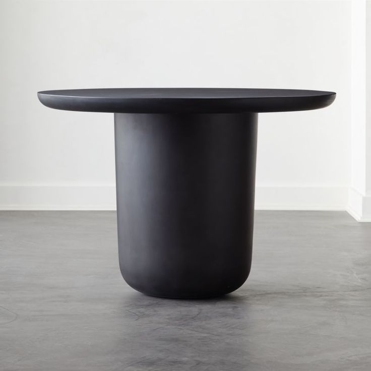 a black round table sitting on top of a cement floor next to a white wall