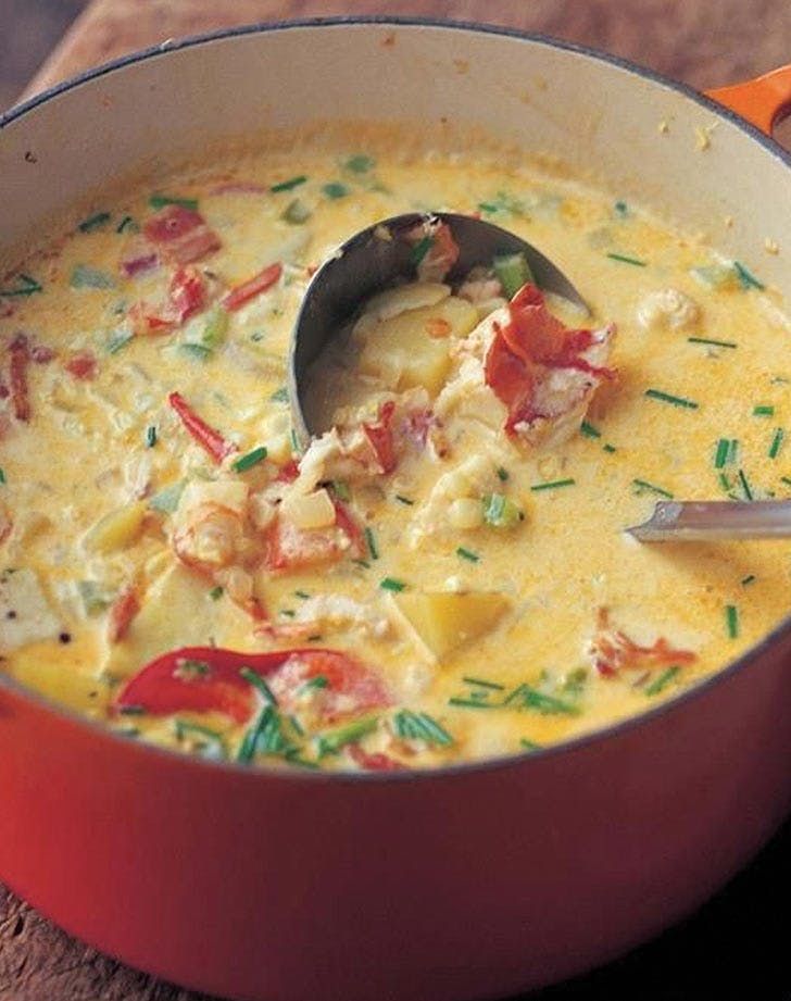 a red pot filled with soup on top of a wooden table next to an orange spoon