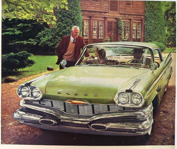 an old man standing next to a green car in front of a house with ivy growing on it