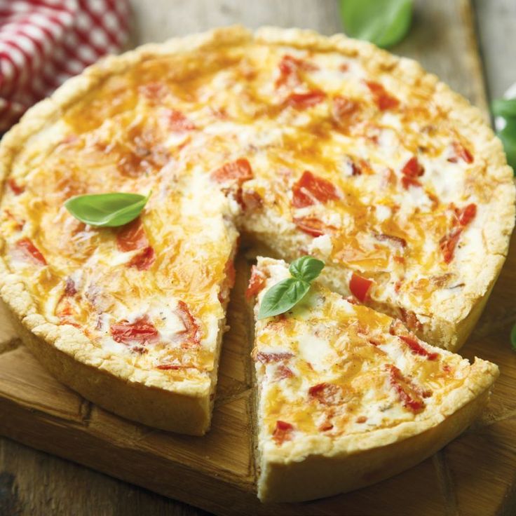 a cheese and tomato quiche on a wooden cutting board with one slice cut out