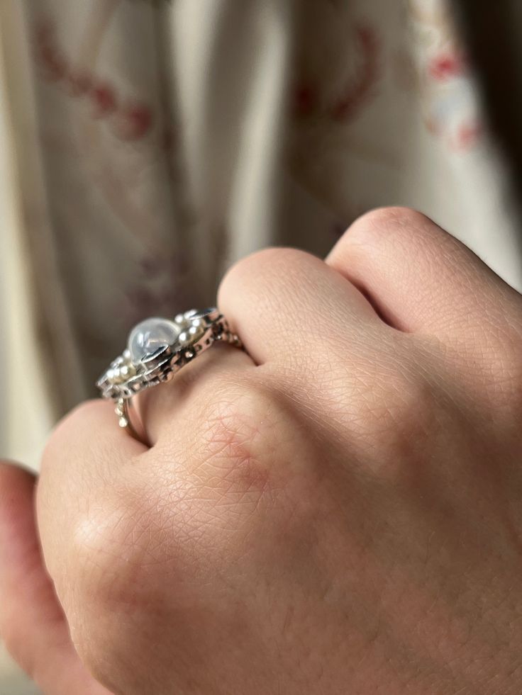 “Art Deco” was an era marked by extravagance and innovation. The Art Deco style itself was an eclectic mix of heavy geometric shapes, with curved ornamental elements. The resulting silhouettes were often monolithic but elegant, with applied decorative elements. This Moonstone and Sapphire Edwardian Conversion Ring is a wonderful example of this iconic Art Deco style. Crafted in 20 carat white gold, this ring immediately captures the gaze with its dazzling array of miniature pearls and sapphire stones haloing a truly luminescent cabochon moonstone. What makes this treasure particularly special is that it is a conversion piece; the beautiful moonstone center was once part of an antique brooch. Now, with the use of a 14 carat gold replica shank, it has been transformed into the glorious ring Elegant White Gold Dome Ring With Open Band, Elegant Silver Dome Ring With Open Band, Elegant Metal Dome Ring As Gift, Elegant Metal Dome Ring Perfect For Gifts, Elegant Metal Dome Ring For Gift, Elegant Adjustable Open Band Dome Ring, Elegant Metal Dome Ring Gift, Elegant White Gold Dome Ring With Rose Cut Diamonds, Elegant Metal Dome Ring With Polished Finish