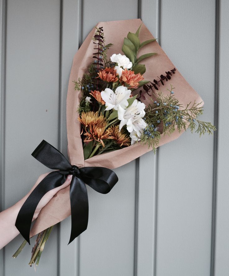 a bouquet of flowers is tied to a wall with a black ribbon and someone's hand holding it