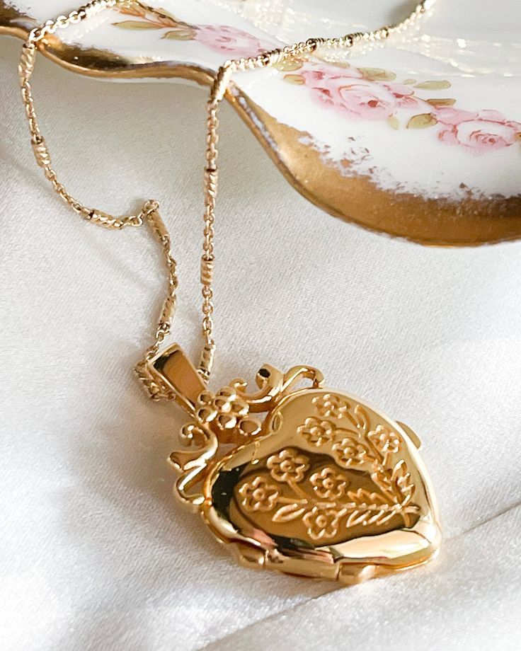 The Jardin Locket Necklace is a vintage inspired heart floral locket.18kt Gold plated silver functioning locket measuring 25mm L x 20mm W x 6.7mm thick. And 9.3 g in weight. The chain is made of gold plated silver measuring 20 inches in length. Vintage Round Pendant Charm Necklace, Medallion Locket Necklace For Keepsakes, Vintage Gold Necklaces With Heart Charm, Gold Necklace With Heart Charm For Vintage Collection, Elegant Flower Pendant Locket Necklace For Keepsakes, Heirloom Pendant Locket Necklace With Charms, Gift Locket Pendant Necklace, Vintage Heart Pendant Charm Necklace, Elegant Pendant Locket Necklace With Vintage Charm